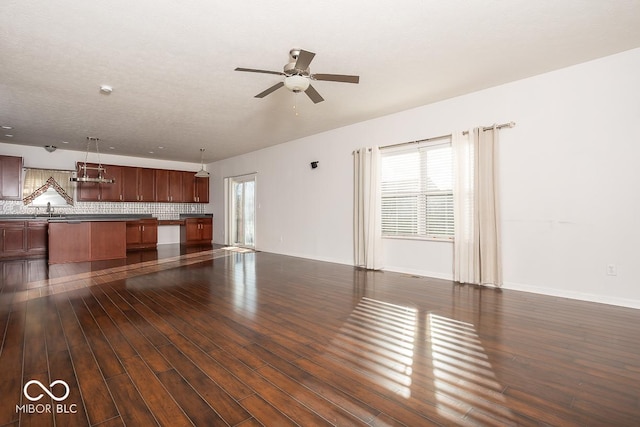 unfurnished living room featuring ceiling fan, baseboards, dark wood finished floors, and a sink