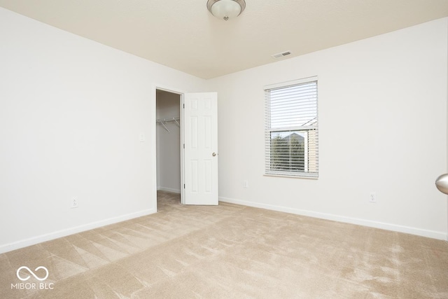 unfurnished bedroom featuring light carpet, visible vents, baseboards, a walk in closet, and a closet