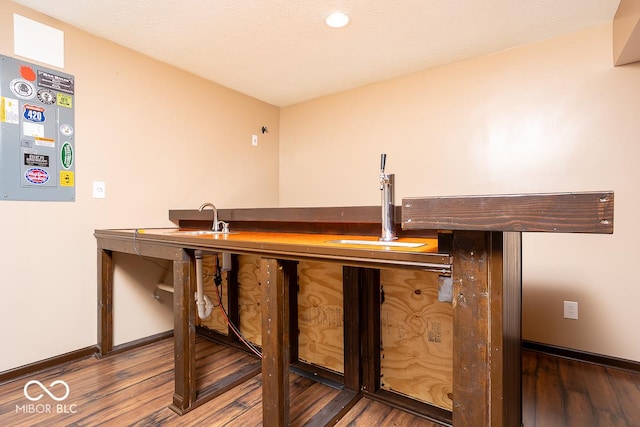 bar featuring a textured ceiling, indoor wet bar, wood finished floors, and baseboards