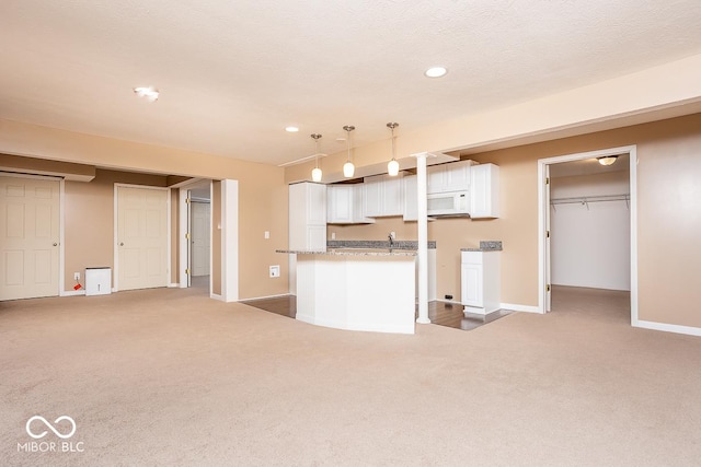 kitchen with white microwave, white cabinets, a textured ceiling, and light colored carpet