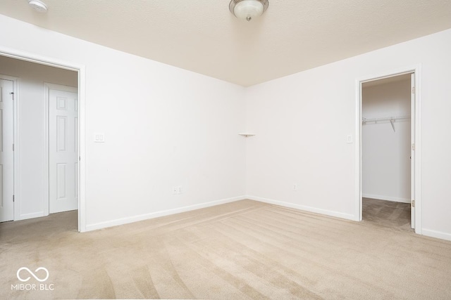 unfurnished bedroom with a textured ceiling, light colored carpet, baseboards, a closet, and a walk in closet