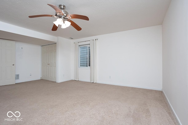 empty room featuring light colored carpet, visible vents, a textured ceiling, and baseboards