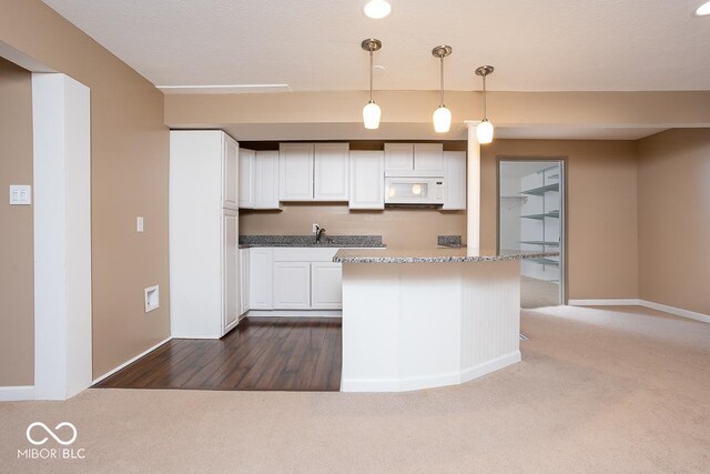 kitchen featuring decorative light fixtures, white microwave, white cabinets, a kitchen island, and baseboards