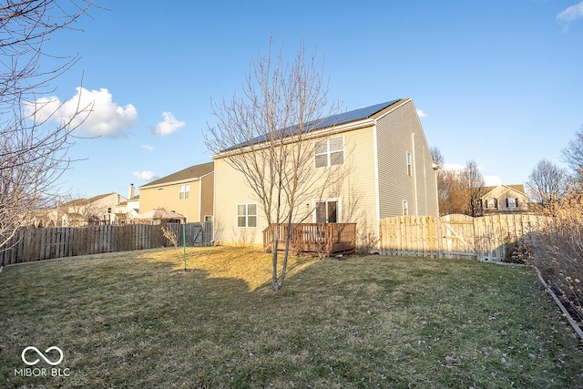 back of property with a deck, a yard, a fenced backyard, and roof mounted solar panels