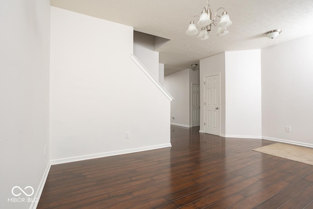 spare room with a textured ceiling, dark wood-style flooring, baseboards, and an inviting chandelier