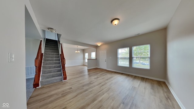 unfurnished living room with a chandelier and light wood-type flooring