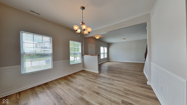 unfurnished dining area featuring light wood-type flooring, plenty of natural light, and a notable chandelier