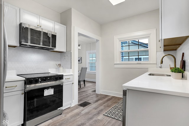 kitchen with white cabinetry, sink, light hardwood / wood-style flooring, stove, and decorative backsplash