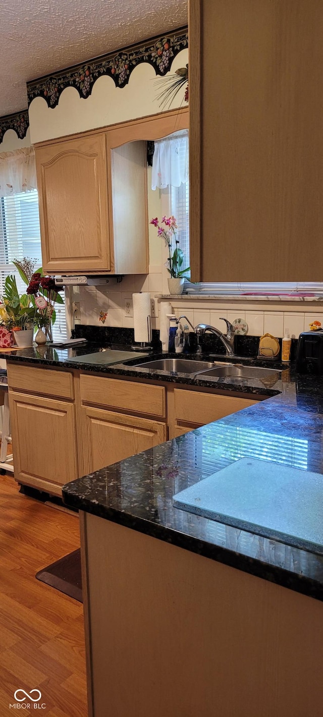 kitchen with sink, dark stone counters, light hardwood / wood-style floors, a textured ceiling, and decorative backsplash