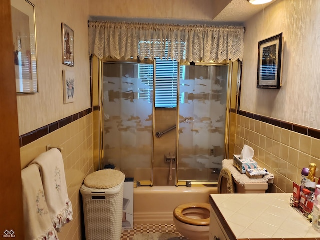 full bathroom with vanity, toilet, tile walls, and bath / shower combo with glass door