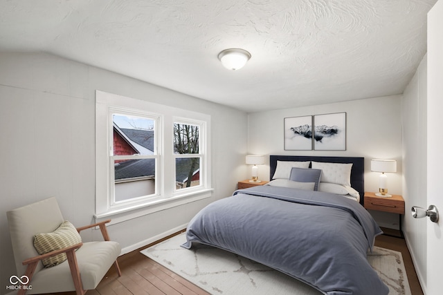 bedroom featuring wood-type flooring, a textured ceiling, and lofted ceiling