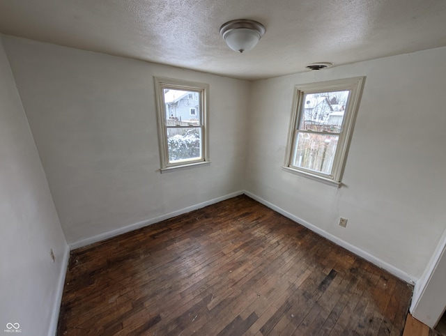 empty room featuring a textured ceiling, dark hardwood / wood-style floors, and plenty of natural light