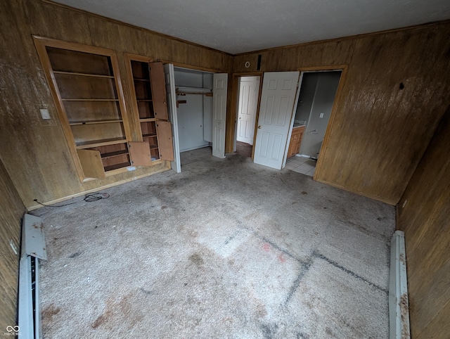 unfurnished bedroom featuring wooden walls, light colored carpet, and a baseboard heating unit