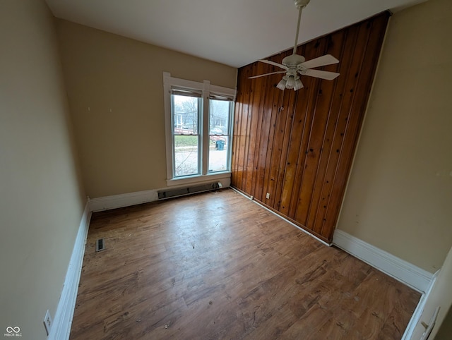 unfurnished room with hardwood / wood-style flooring, ceiling fan, and wooden walls