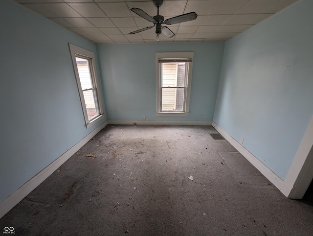 empty room with a paneled ceiling, ceiling fan, and a healthy amount of sunlight