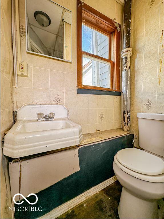 bathroom with toilet, tile walls, and sink