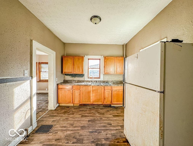 kitchen featuring a textured ceiling, white refrigerator, dark wood-type flooring, and sink