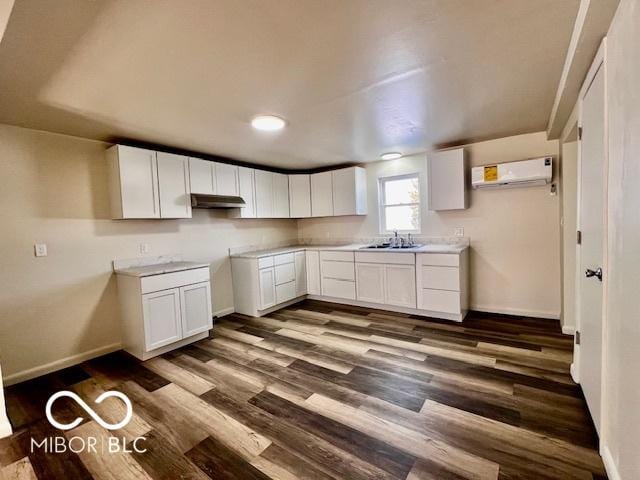 kitchen with dark wood-type flooring, white cabinetry, a wall mounted AC, and sink