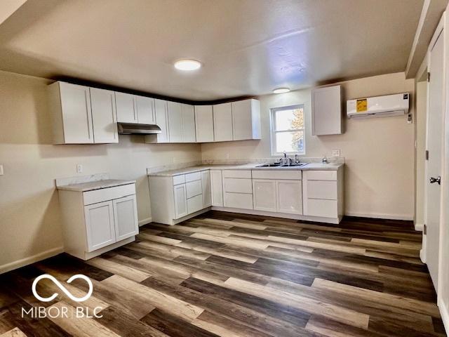 kitchen featuring white cabinets, dark wood-type flooring, sink, and a wall unit AC