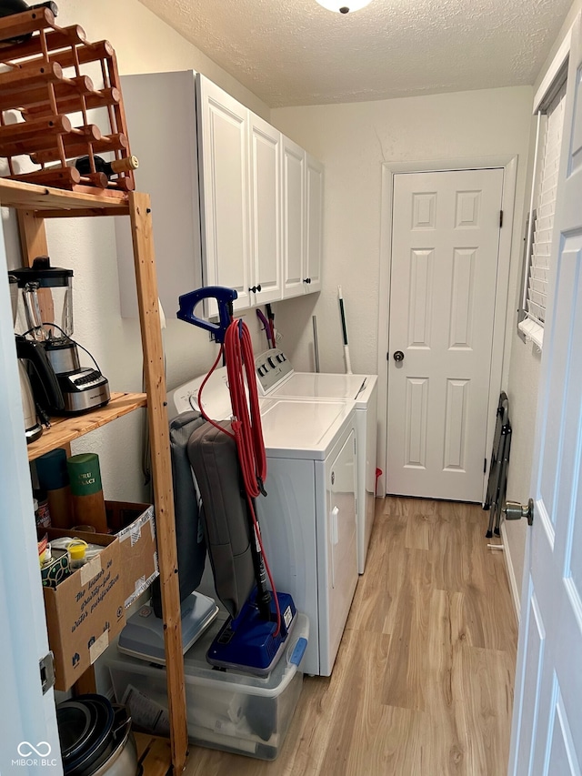 washroom with washer and dryer, cabinets, light wood-type flooring, and a textured ceiling