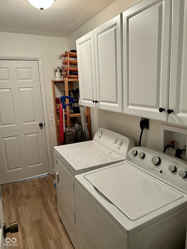 laundry room with washing machine and clothes dryer, cabinets, light hardwood / wood-style floors, and a textured ceiling