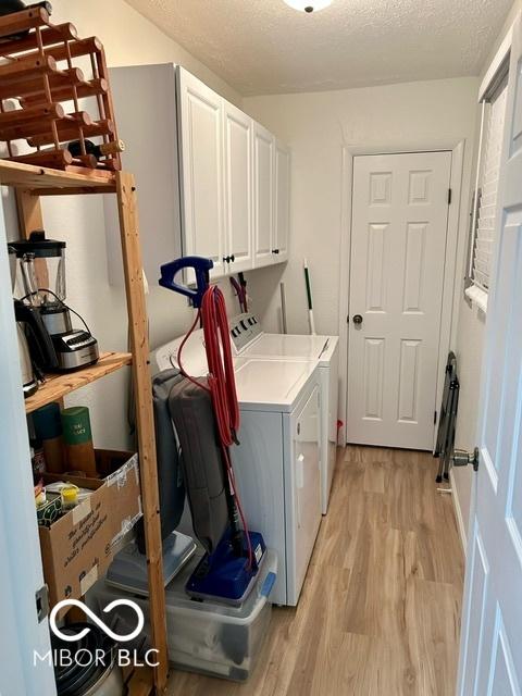 laundry room with cabinet space, light wood-style flooring, a textured ceiling, and washing machine and dryer