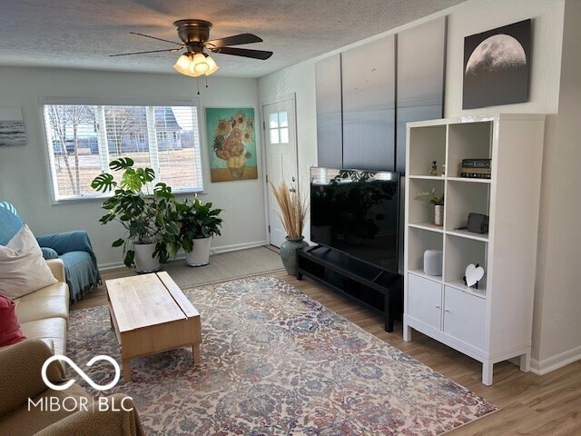 living room with ceiling fan, a textured ceiling, baseboards, and wood finished floors