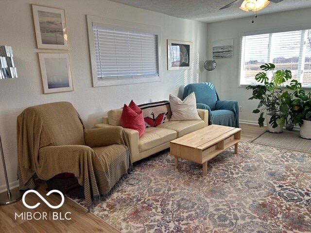 living area with a textured ceiling, ceiling fan, wood finished floors, and baseboards