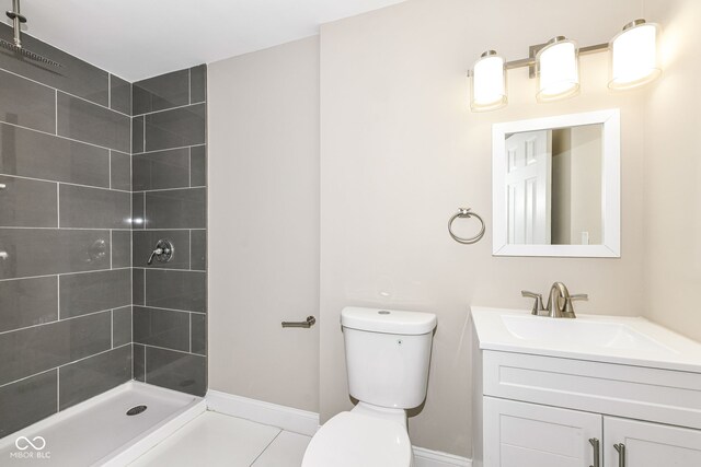 bathroom with tiled shower, tile patterned flooring, vanity, and toilet