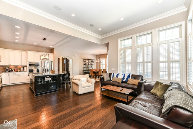 living room with dark wood-type flooring, a chandelier, crown molding, and a wealth of natural light