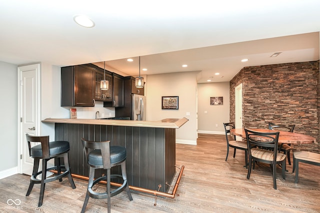 kitchen featuring hanging light fixtures, stainless steel fridge, kitchen peninsula, light wood-type flooring, and a breakfast bar area