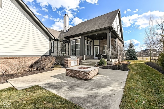 rear view of property with an outdoor fire pit, a lawn, a patio, a chimney, and brick siding