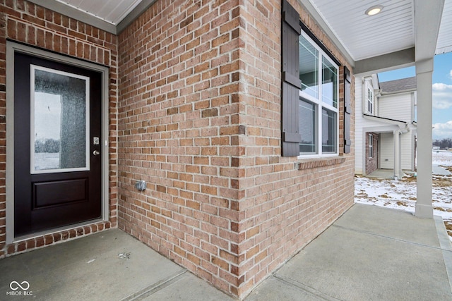 snow covered property entrance featuring brick siding