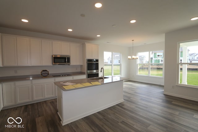 kitchen featuring a kitchen island with sink, dark wood-type flooring, white cabinets, decorative light fixtures, and stainless steel appliances