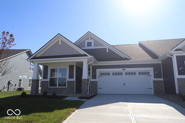 craftsman house featuring covered porch, a garage, central air condition unit, and a front lawn