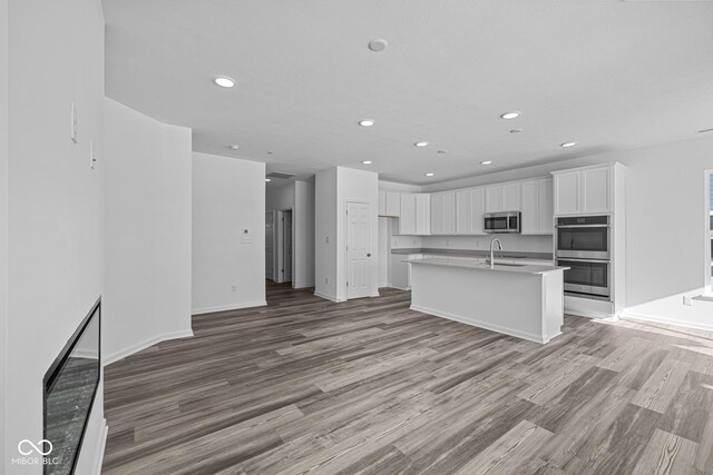 kitchen with appliances with stainless steel finishes, light hardwood / wood-style flooring, white cabinets, sink, and a kitchen island with sink