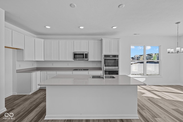 kitchen featuring appliances with stainless steel finishes, decorative light fixtures, a kitchen island with sink, and white cabinets