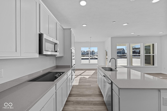 kitchen with appliances with stainless steel finishes, light hardwood / wood-style flooring, sink, white cabinetry, and a kitchen island with sink