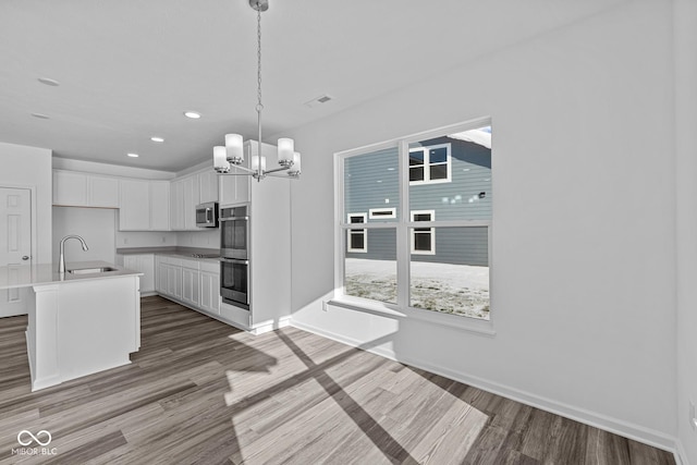 kitchen featuring sink, white cabinetry, stainless steel appliances, hanging light fixtures, and a kitchen island with sink