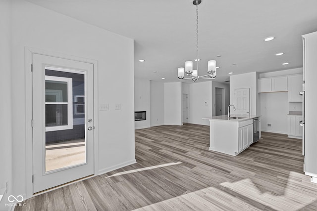 kitchen featuring a center island with sink, light hardwood / wood-style floors, pendant lighting, sink, and white cabinetry