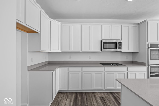 kitchen with white cabinets, appliances with stainless steel finishes, a textured ceiling, and dark hardwood / wood-style floors