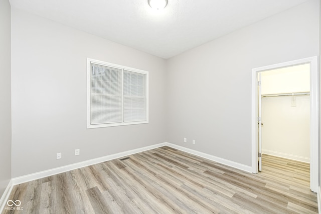 unfurnished bedroom with a closet, a spacious closet, and light hardwood / wood-style flooring