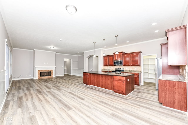 kitchen with hanging light fixtures, light hardwood / wood-style floors, a kitchen island with sink, appliances with stainless steel finishes, and ornamental molding