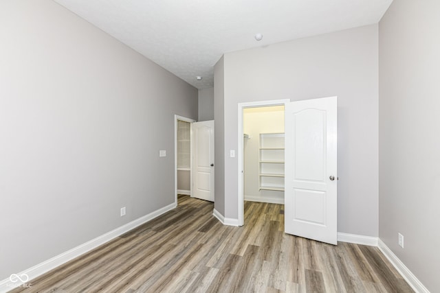 unfurnished bedroom featuring a walk in closet, light wood-type flooring, a textured ceiling, a towering ceiling, and a closet