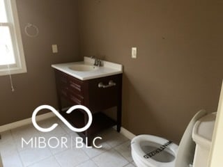 half bath with tile patterned floors, vanity, toilet, and baseboards