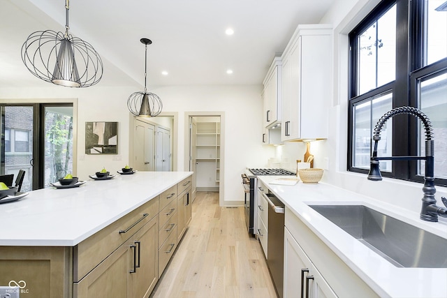 kitchen featuring sink, stainless steel appliances, a large island, white cabinetry, and hanging light fixtures