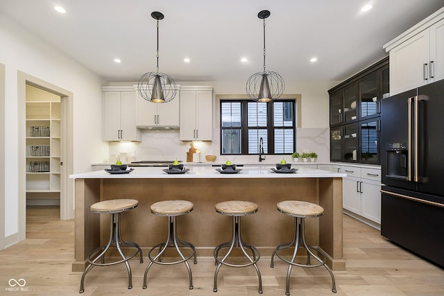 kitchen with a kitchen island, white cabinets, hanging light fixtures, and high end black fridge