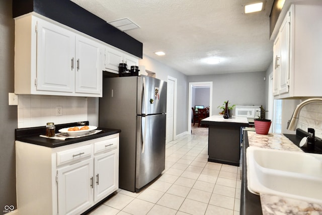 kitchen featuring sink, white cabinetry, a center island, decorative backsplash, and stainless steel refrigerator