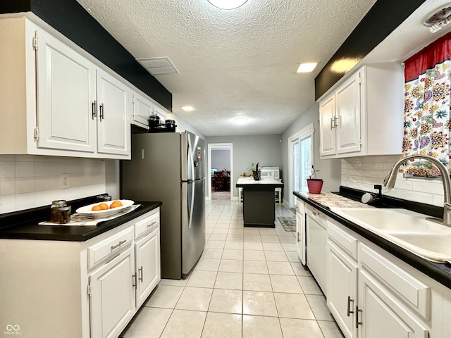 kitchen with stainless steel refrigerator, light tile patterned floors, decorative backsplash, sink, and white cabinetry