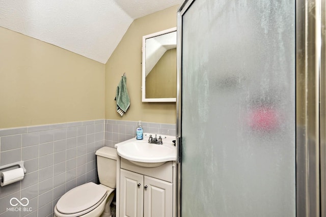 bathroom featuring vanity, a textured ceiling, vaulted ceiling, tile walls, and toilet